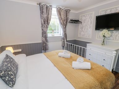 A bedroom with a white metal bed with a mustard blanket and white towels in front of a window with gray curtains at Horeb Chapel House in Tanygrisiau