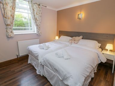A bedroom with two single beds with white linens bedside lamps and a window with floral curtains at Horeb Chapel House in Tanygrisiau