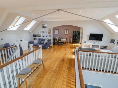A loft living area with sofas dining table TV and wooden floor at Horeb Chapel House in Tanygrisiau