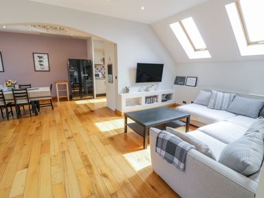 A living room with a gray sectional sofa a black coffee table and a mounted TV next to a dining area with a table and chairs at Horeb Chapel House in Tanygrisiau