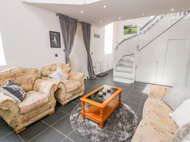 A living room with patterned sofas a wooden coffee table on a round rug and a staircase in the background at Horeb Chapel House in Tanygrisiau
