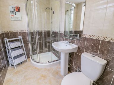 A bathroom with a glass shower enclosure a white sink with a mirror above a white toilet and a small shelf unit at Horeb Chapel House in Tanygrisiau