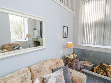 A living room with a patterned sofa and cushions a lamp on a tree stump table firewood in a basket and a window with blinds at Horeb Chapel House in Tanygrisiau