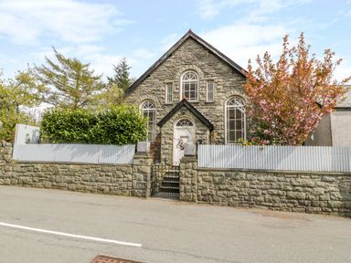 Exterior view of a stone house with arched windows and a gate in front at Horeb Chapel House in Tanygrisiau