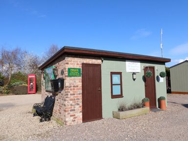 An outdoor building with two brown doors and a bench on a gravel area at Lake View Lodge in Marston near Barkston