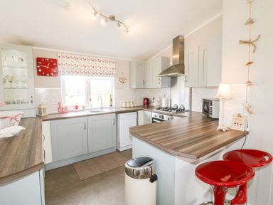 A kitchen with light blue cabinets a wooden countertop a window with patterned blind and red stools at a counter at Lake View Lodge in Marston near Barkston