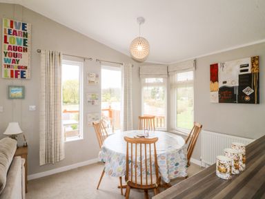 A dining area with a round table covered with a leaf patterned tablecloth and four wooden chairs at Lake View Lodge in Marston near Barkston