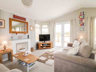 A living room with two sofas a coffee table a TV on a stand and decor at Lake View Lodge in Marston near Barkston
