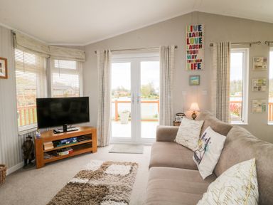 A living room with a sofa a TV on a stand and a rug at Lake View Lodge in Marston near Barkston
