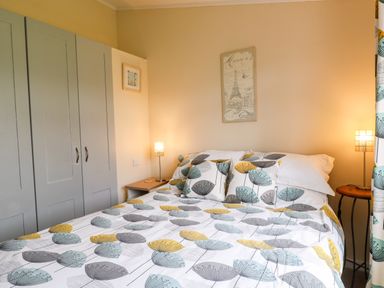A bedroom with a bed with patterned bedding two bedside tables with lamps and a wardrobe at Lake View Lodge in Marston near Barkston