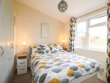 A bedroom with a double bed bedside tables lamps built in wardrobes and a window with patterned curtains at Lake View Lodge in Marston near Barkston