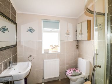 A bathroom with a toilet a sink a mirror a window and a glass shower enclosure at Lake View Lodge in Marston near Barkston