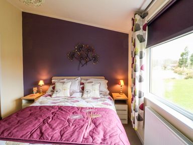 A bedroom with a bed with floral bedding and two bedside tables with lamps at Lake View Lodge Marston near Barkston