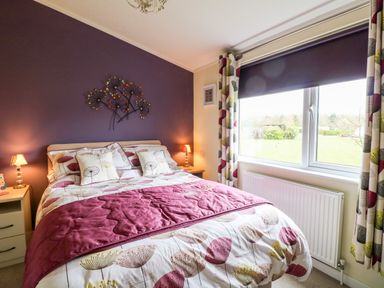 A bedroom with a bed with floral bedding two bedside tables with lamps a window with curtains and a radiator at Lake View Lodge Marston near Barkston
