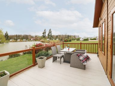 A wooden deck with a table and chairs overlooking a grassy area and a lake at Lake View Lodge in Marston near Barkston