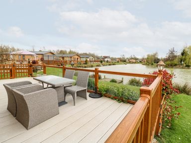 An outdoor deck with table and chairs overlooking a lake with lodges in the background at Lake View Lodge Marston near Barkston