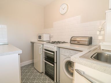 A kitchen with a microwave on a countertop a gas stove an oven a washing machine a bread box and a sink at Holly Cottage in Criccieth