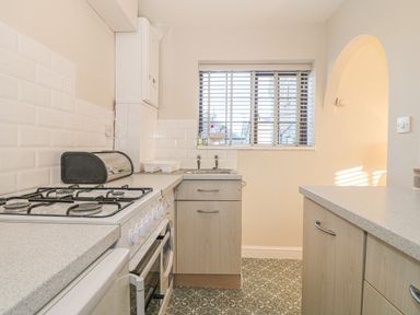A kitchen with a gas stove a bread box a sink under a window and cabinets at Holly Cottage in Criccieth