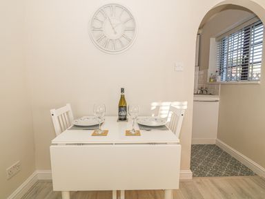 A small dining table set for two with plates and wine glasses next to an archway leading to a kitchen at Holly Cottage in Criccieth