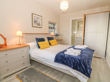 A bedroom with a double bed, bedside tables with lamps, wardrobe, and an en suite bathroom at Holly Cottage in Criccieth