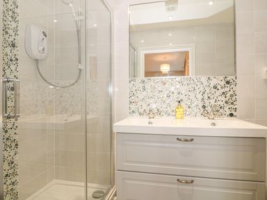 A bathroom with a glass shower enclosure and a double sink vanity at Holly Cottage in Criccieth