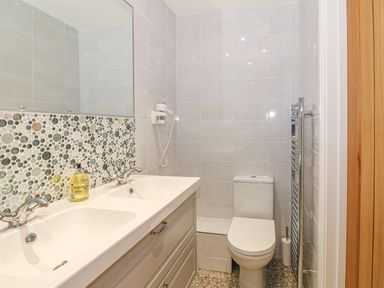A bathroom with a double sink vanity a toilet a wall-mounted hairdryer and a towel heater at Holly Cottage in Criccieth