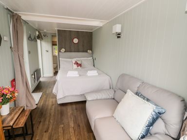 A bedroom with a bed a sofa a clock flowers on a table and a bathroom visible at Hydrangea in Bretforton