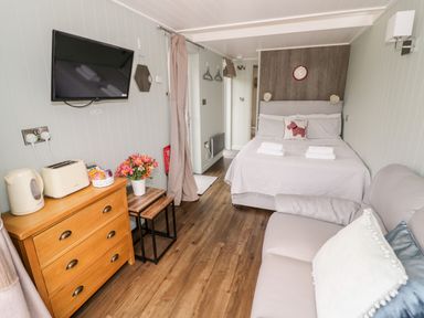A bedroom with a bed sofa wooden dresser kettle toaster wall mounted TV and flowers at Hydrangea Bretforton