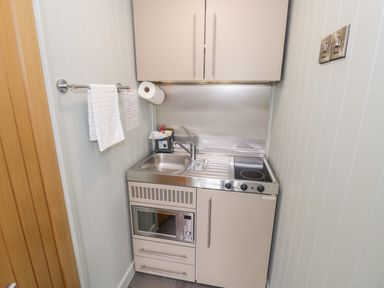 A small kitchenette with a sink stove microwave and cabinets at Hydrangea in Bretforton