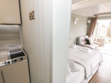 A kitchenette with a stove and a bed with towels and a sofa in a room with an open door at Hydrangea in Bretforton