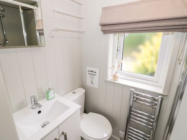A bathroom with a white sink, a toilet, a window with a blind, and a heated towel rail at Hydrangea in Bretforton