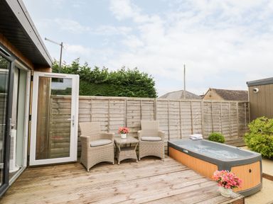 An outdoor wooden deck with two wicker chairs a small table with flowers a hot tub and a wooden fence at Hydrangea in Bretforton