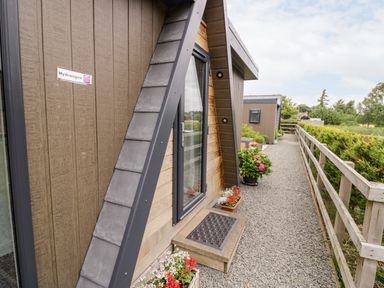 A gravel pathway alongside a wooden building with potted flowers and a wooden fence at Hydrangea Bretforton