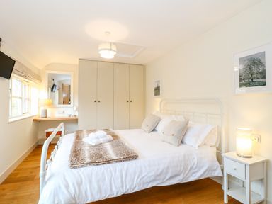 A bedroom with a white metal bed frame a bedside table with a lamp a wardrobe and a desk by the window at Shippon Barn in Yeovil