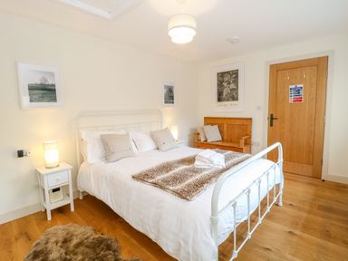 A bedroom with a white metal bed frame a wooden bench two framed pictures and a wooden door at Shippon Barn in Yeovil