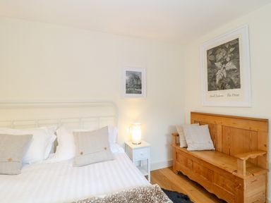 A bedroom with a white bed a bedside table with a lamp and a wooden bench with cushions at Shippon Barn in Yeovil
