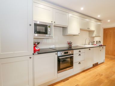 A kitchen with white cabinets black countertop built in oven microwave and a sink at Shippon Barn in Yeovil