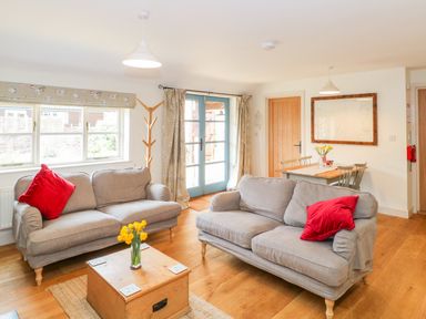 A living room with two grey sofas with red cushions a wooden coffee table with flowers and a dining table with chairs at Shippon Barn in Yeovil