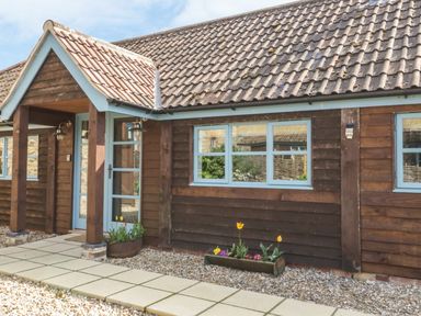 The exterior of a building with wooden cladding blue framed windows a tiled roof and flower planters on a gravel ground at Shippon Barn in Yeovil
