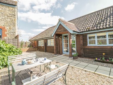 A small outdoor patio with a table and benches in front of a wooden building at Shippon Barn in Yeovil