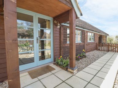 A wooden house exterior with light blue double doors and flower beds on the side at Shippon Barn in Yeovil