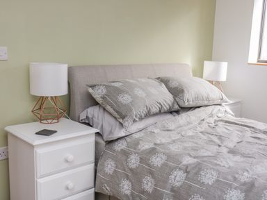 A bedroom with a bed with patterned bedding and two white bedside tables with lamps at Black Cat Bach in Gilwern
