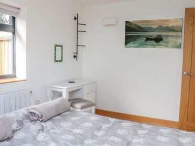 A bedroom with a bed with rolled towels a small white desk with a stool a mirror a wall rack and a landscape picture at Black Cat Bach in Gilwern