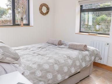A bedroom with a bed covered with patterned bedding and two rolled towels placed on top at Black Cat Bach in Gilwern