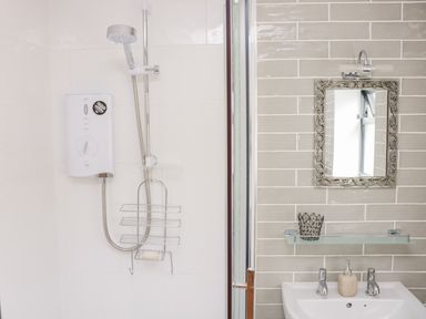 A bathroom with a shower unit and shower head on a white tiled wall and a sink with a mirror above it at Black Cat Bach in Gilwern