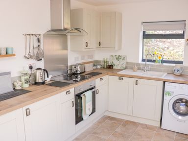 A kitchen with white cabinets wooden countertops a kettle toaster oven sink washing machine and utensils hanging on the wall at Black Cat Bach in Gilwern