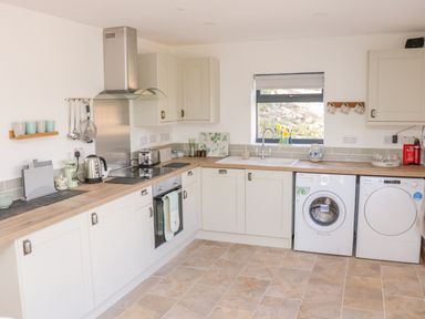A kitchen with white cabinets wooden countertops a washing machine dishwasher oven and a window at Black Cat Bach in Gilwern