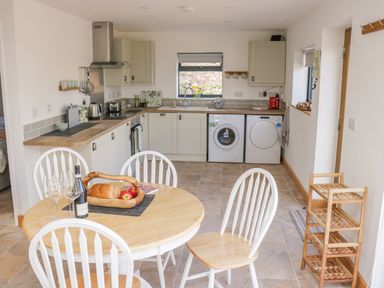 A kitchen with a round wooden dining table and chairs washing machine and dryer under a window at Black Cat Bach in Gilwern