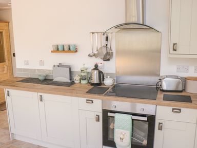 A kitchen with wooden countertop white cabinets electric stove oven kettle toaster and hanging utensils at Black Cat Bach in Gilwern
