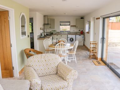 An open plan kitchen and dining area with a round table and chairs a patterned armchair and sliding glass doors at Black Cat Bach in Gilwern